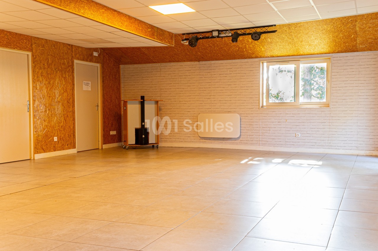 Salle vide avec sol en carrelage, murs en bois et briques blanches, fenêtre laissant entrer la lumière naturelle.