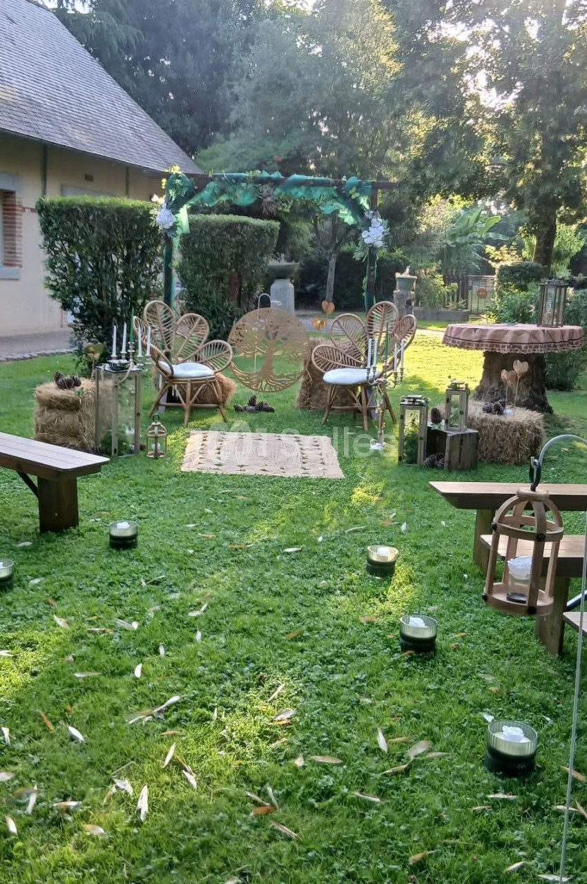 Espace extérieur aménagé pour une cérémonie, avec chaises en rotin, arche décorée et lanternes sur pelouse.
