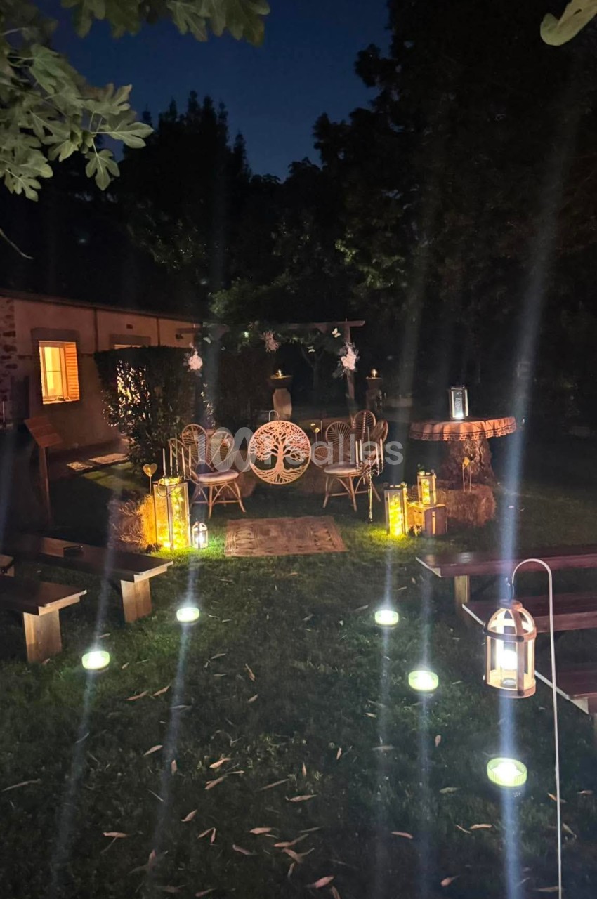 Espace extérieur nocturne décoré avec des lanternes, des guirlandes lumineuses et un mobilier de jardin en rotin.