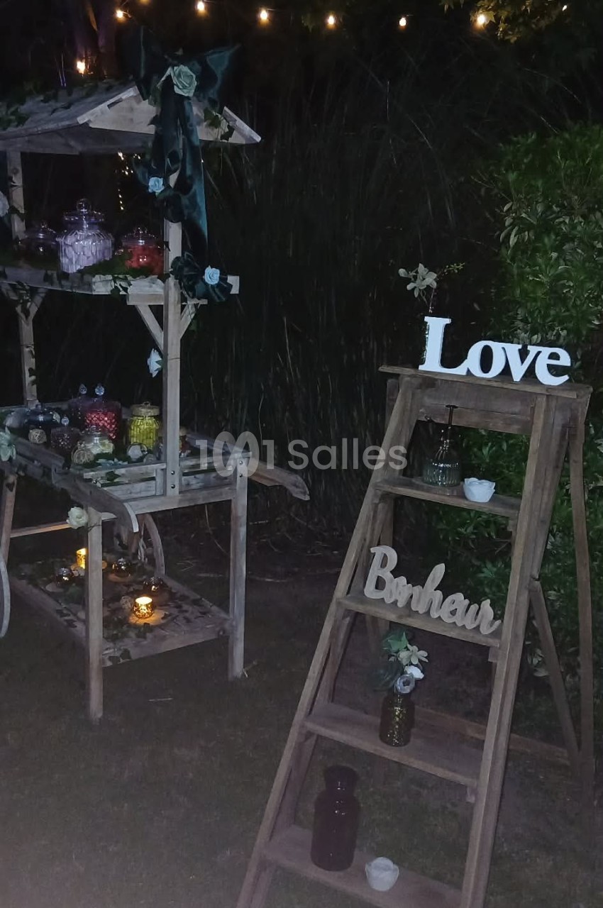 Décoration nocturne avec une échelle en bois portant les mots ’Love’ et ’Bonheur’, et un stand orné de lumières et fleurs.