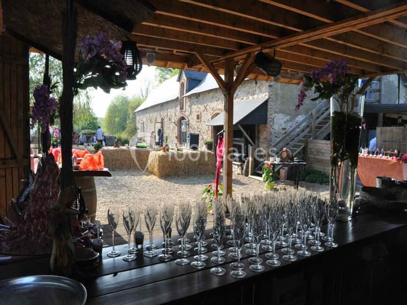 Vue d'une cour rustique avec des tables décorées, des bottes de paille et des verres alignés sur un comptoir en bois.