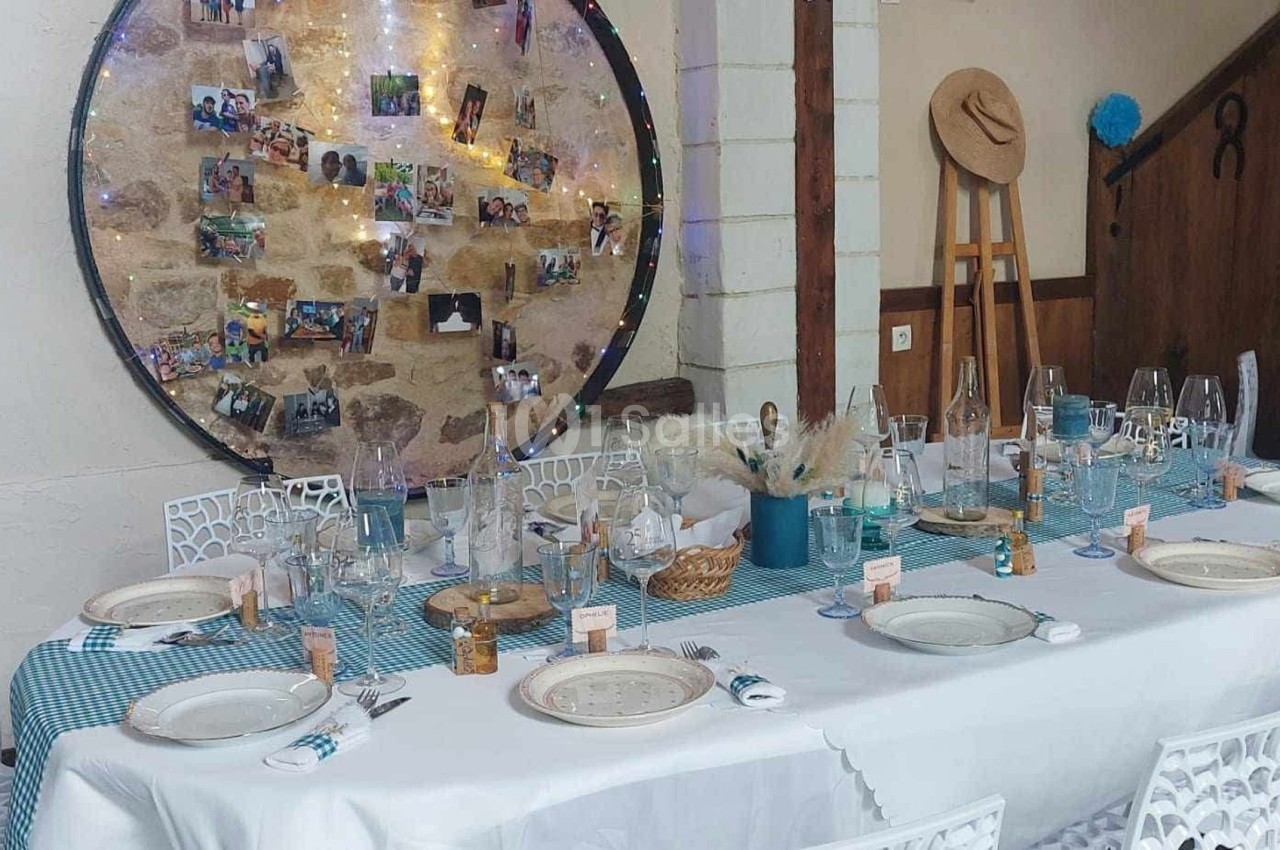 Table dressée pour un repas festif avec nappes bleues, décorations rustiques et un panneau de photos en arrière-plan.