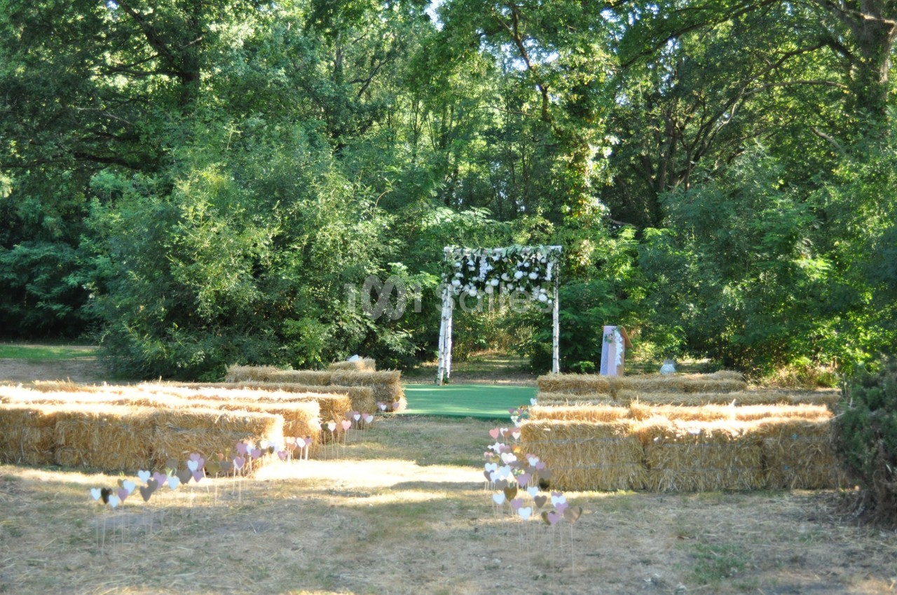 Allée centrale bordée de bottes de paille menant à une arche fleurie dans un cadre naturel verdoyant.