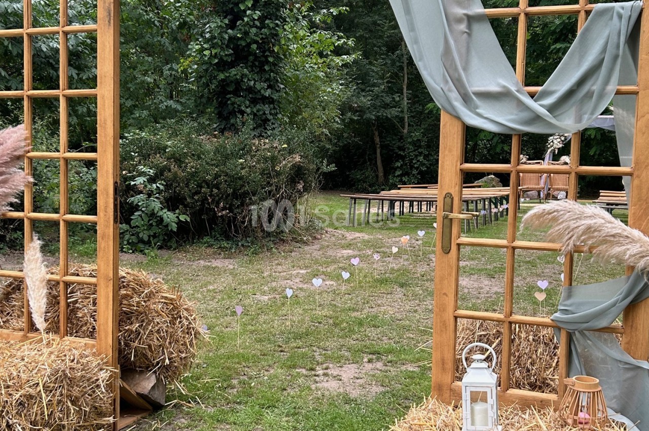 Entrée décorative en bois avec rideaux et bottes de paille, donnant sur un espace extérieur aménagé pour un événement.