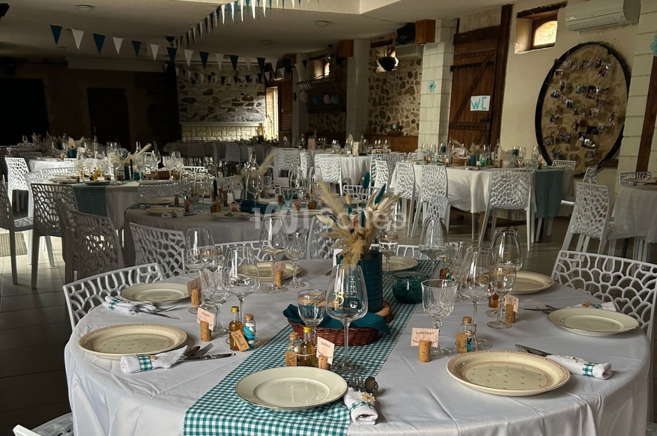 Salle décorée pour un événement avec tables dressées, nappes à carreaux turquoise et éléments rustiques.