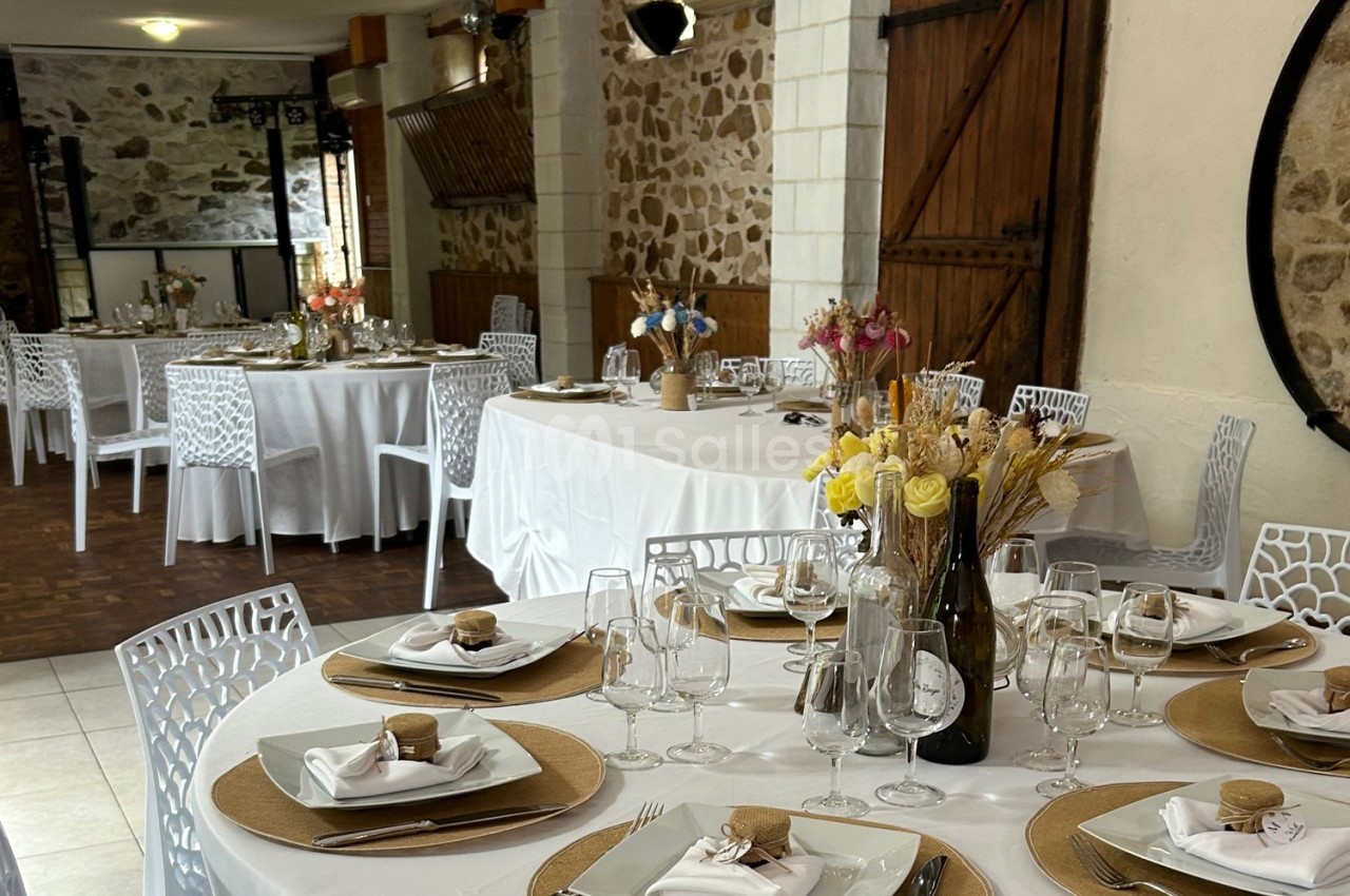 Salle de réception décorée avec des tables dressées, nappes blanches, chaises ajourées et compositions florales.