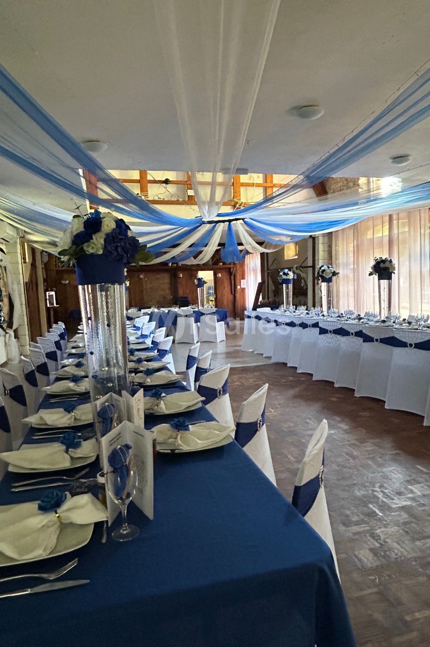 Salle de réception décorée de bleu et blanc avec des tables dressées et des arrangements floraux élégants.