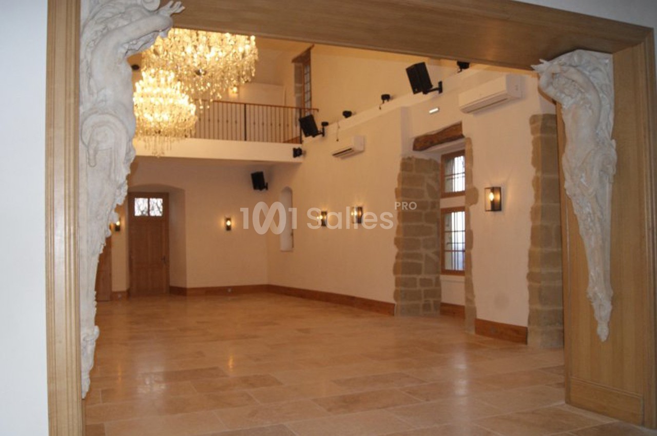 Salle lumineuse avec sol en pierre, lustre imposant, sculptures décoratives et murs ornés de fenêtres et appliques.