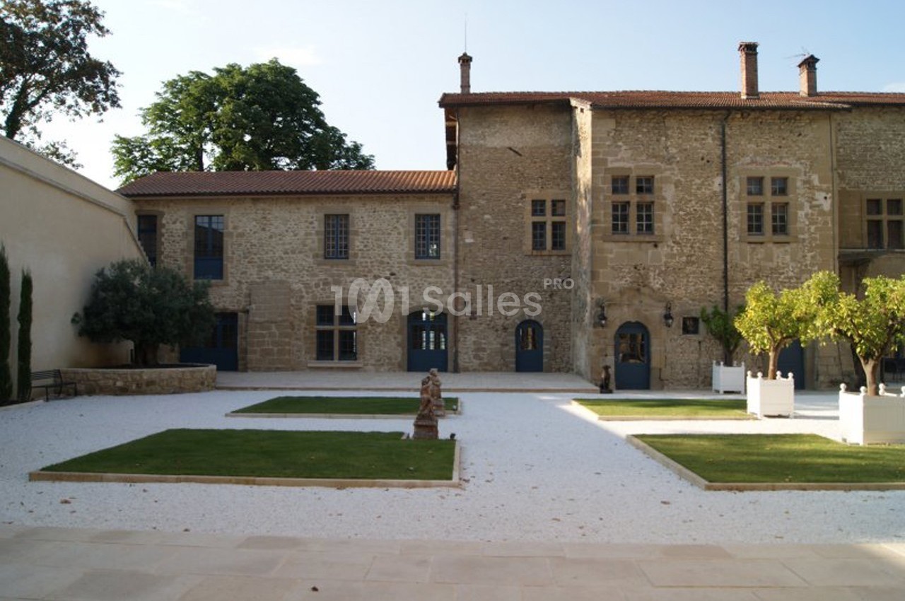 Cour intérieure d'un bâtiment en pierre avec jardin aménagé, arbres en pots et allées gravillonnées.