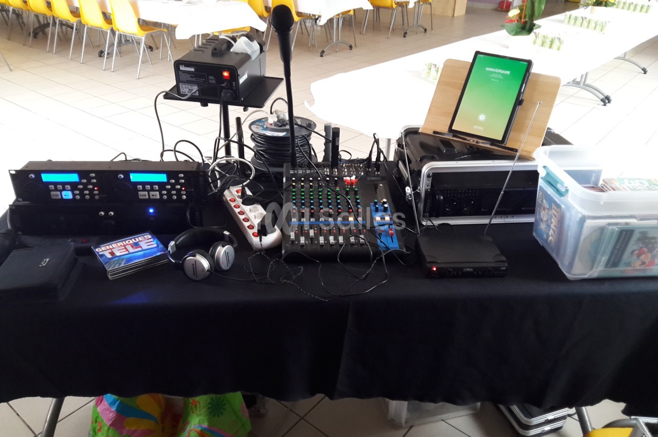 Matériel audio et vidéo installé sur une table, comprenant une console de mixage, un micro, un casque et divers équipements.