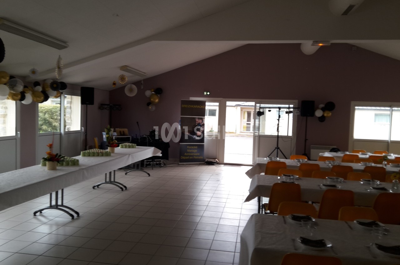 Salle décorée avec des tables dressées, des chaises jaunes et des ballons, prête pour un événement festif.