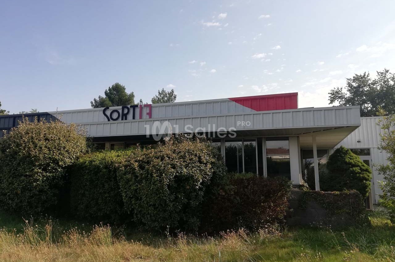 Façade d'un bâtiment commercial avec des arbustes devant et un panneau indiquant ’SORTI’.