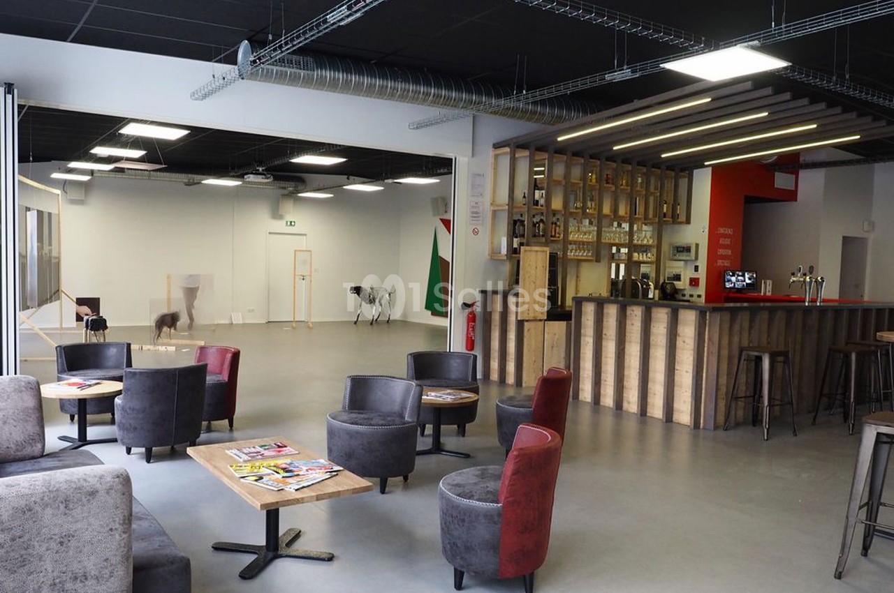Espace intérieur moderne avec coin salon, tables basses, bar en bois et grande salle en arrière-plan.