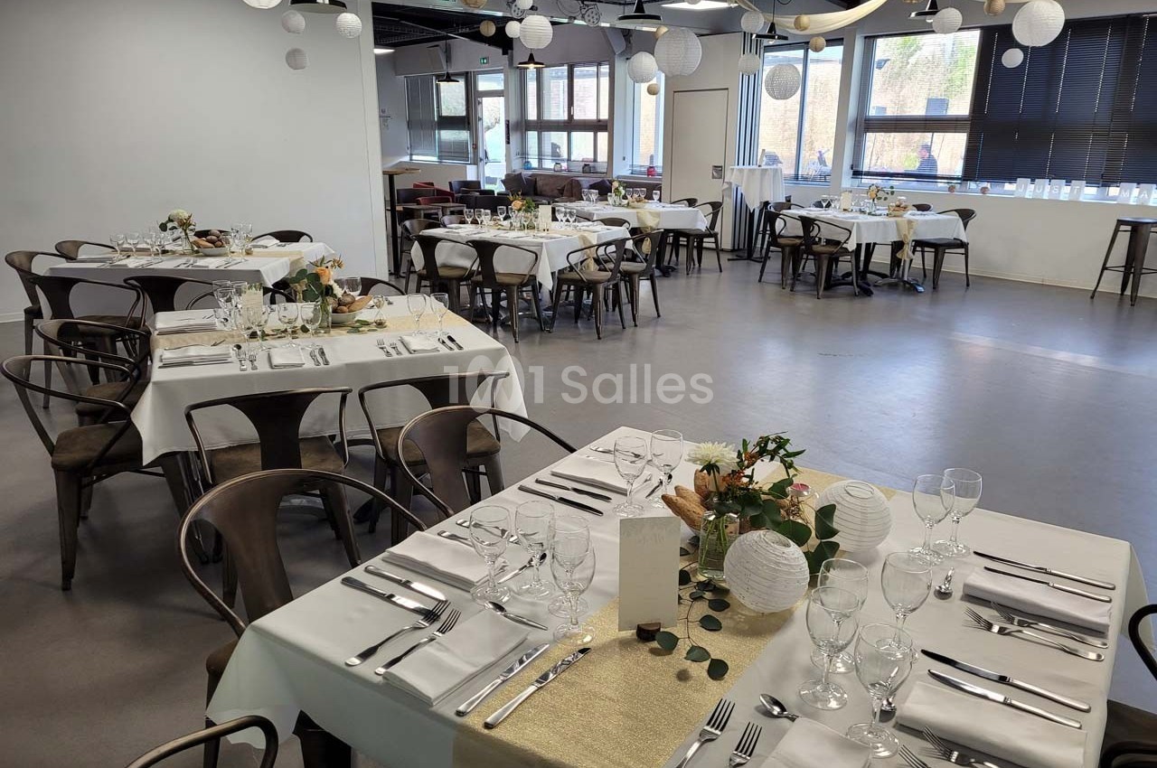 Salle de réception décorée avec des tables dressées, nappes blanches, centres de table floraux et lanternes suspendues.