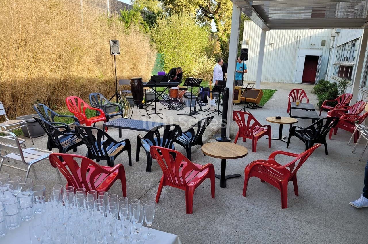 Chaises colorées disposées autour de petites tables sur une terrasse extérieure, avec instruments de musique en arrière-plan.