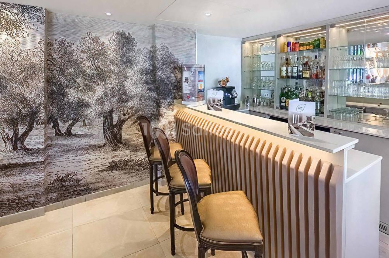 Bar moderne avec comptoir ondulé, trois tabourets et mur décoré d'une fresque représentant un paysage d'oliviers.