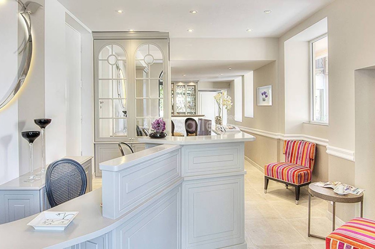 Accueil lumineux avec comptoir blanc, fauteuils colorés, miroir rond éclairé et décoration élégante.