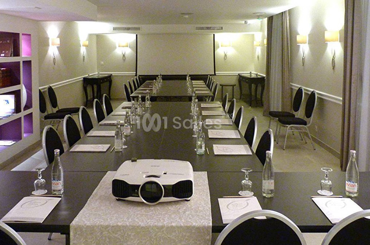Salle de réunion équipée avec une grande table, chaises noires, projecteur et documents disposés pour une présentation.