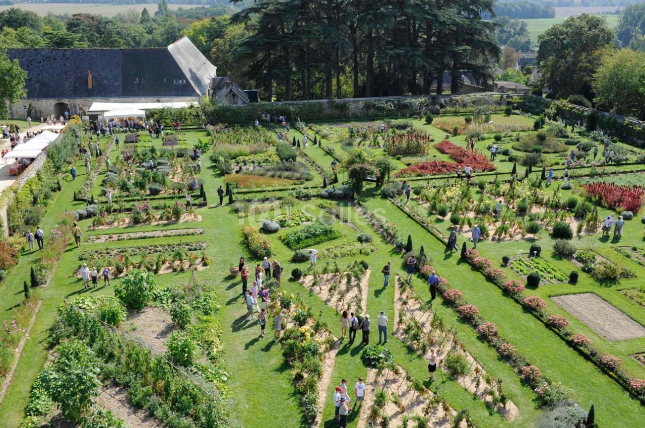 Vue aérienne d'un grand jardin potager avec des visiteurs se promenant parmi les allées et les plantations variées.