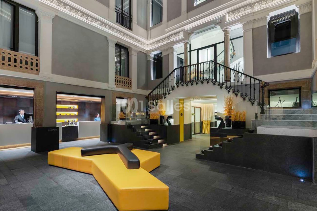 Hall d'entrée moderne avec escalier en fer forgé, comptoir d'accueil et canapé jaune en forme géométrique.
