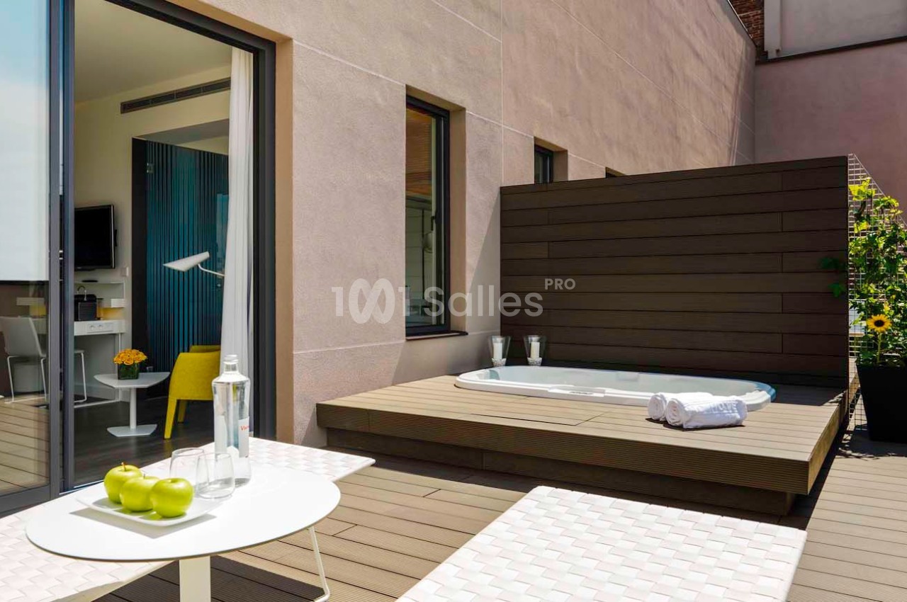Terrasse avec jacuzzi encastré, table avec pommes vertes et serviettes, entourée de murs en bois et en pierre.