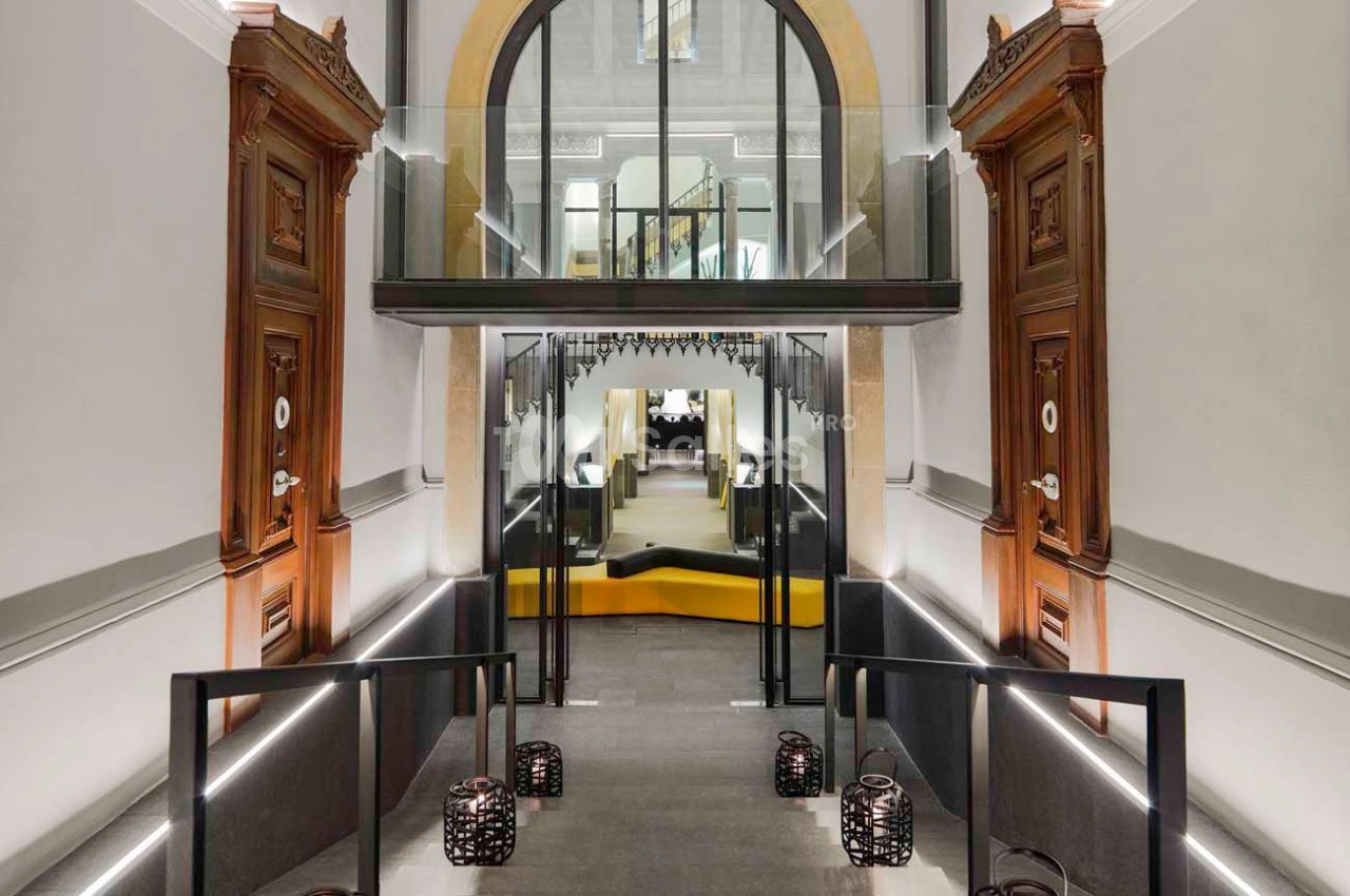 Entrée moderne avec rampes éclairées, portes en bois sculpté et pont en verre menant à un espace intérieur lumineux.