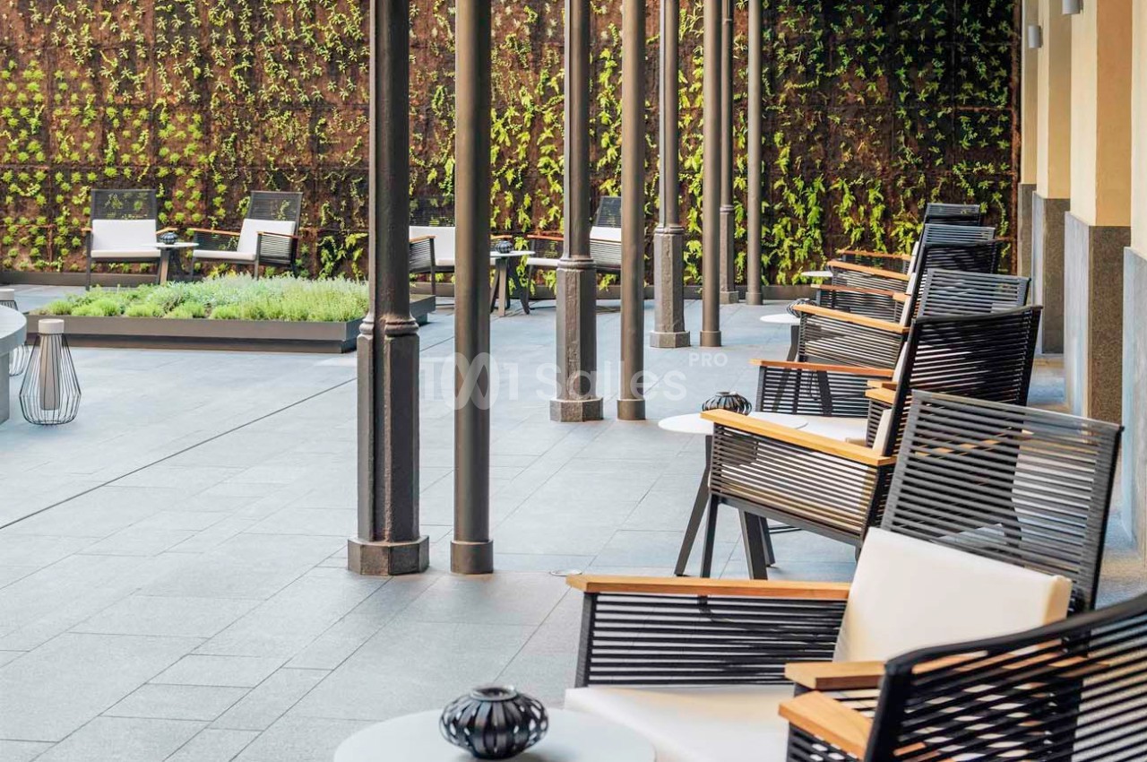 Terrasse avec chaises en bois et métal, tables basses blanches, et mur végétal en arrière-plan.
