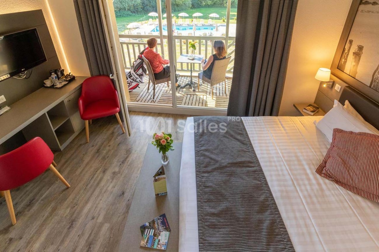 Chambre d'hôtel lumineuse avec lit double, bureau, télévision et balcon donnant sur une piscine extérieure.