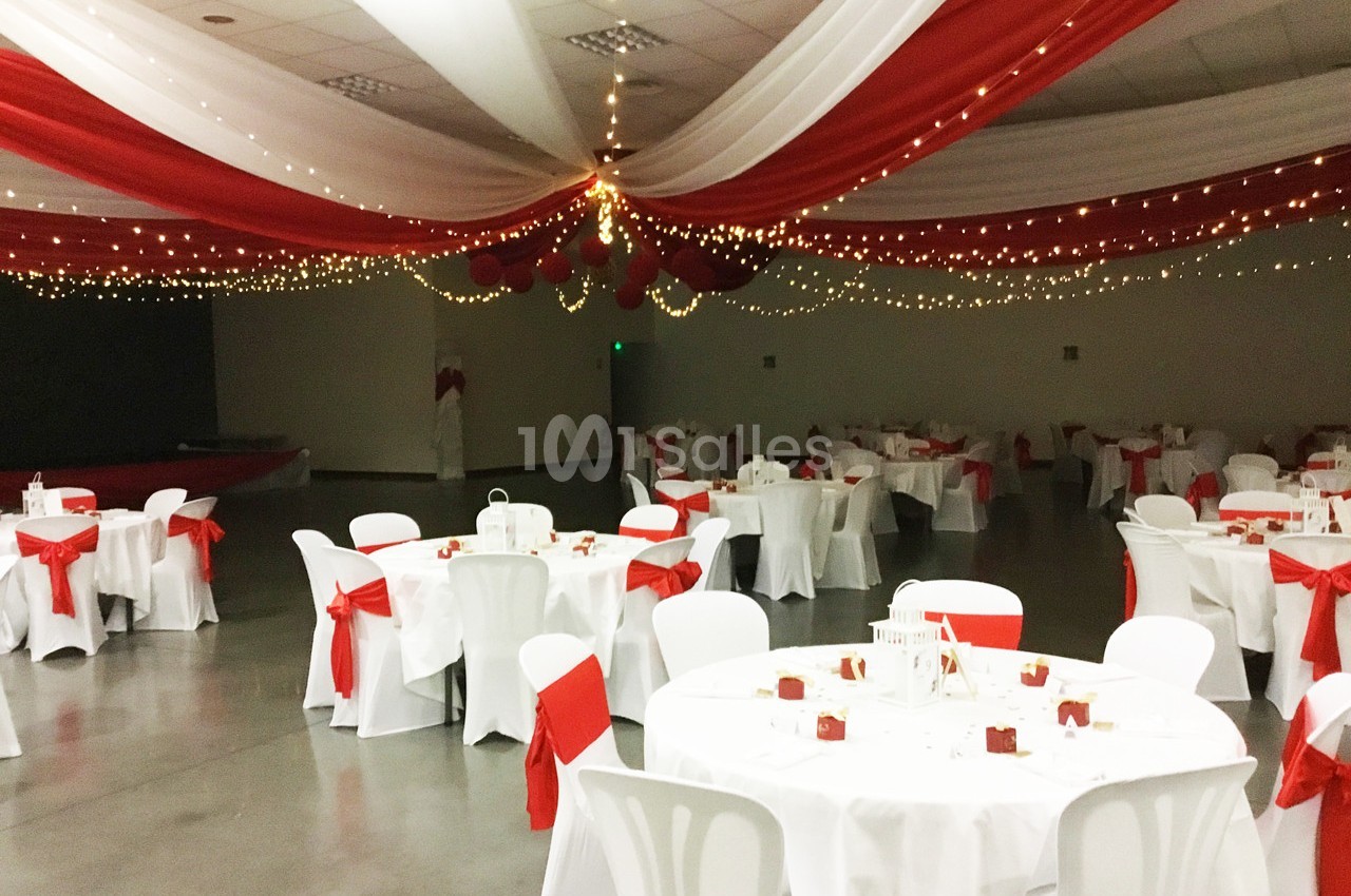 Salle de réception décorée de nappes blanches et rouges, avec des guirlandes lumineuses suspendues au plafond.