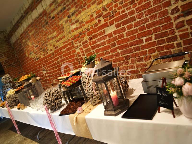 Buffet décoratif avec plats variés, lanternes et éléments rustiques sur une table devant un mur en briques rouges.