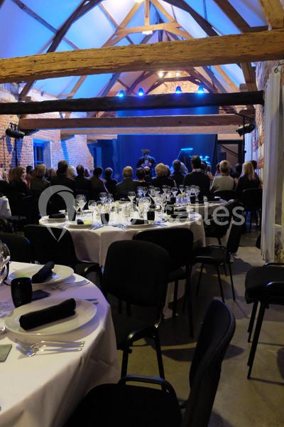 Salle de réception avec tables dressées et invités assis, face à une scène éclairée pour une prestation.