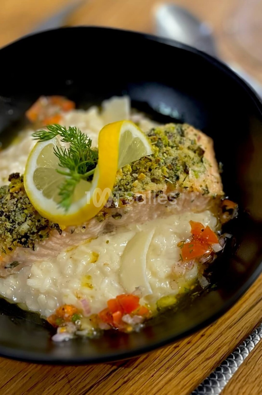 Filet de saumon en croûte d'herbes servi sur un risotto crémeux, garni de citron et d'aneth.