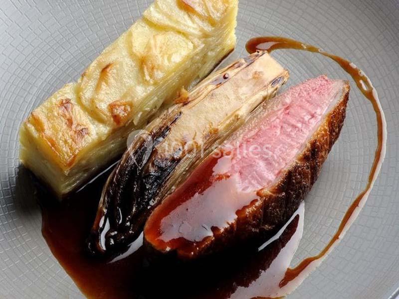 Assiette composée de magret de canard rosé, endive braisée et gratin de pommes de terre, nappée de sauce.
