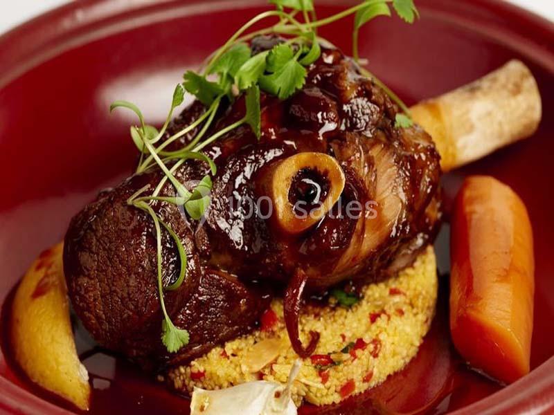 Jarret d'agneau braisé servi sur un lit de couscous avec des légumes et une garniture de fines herbes.