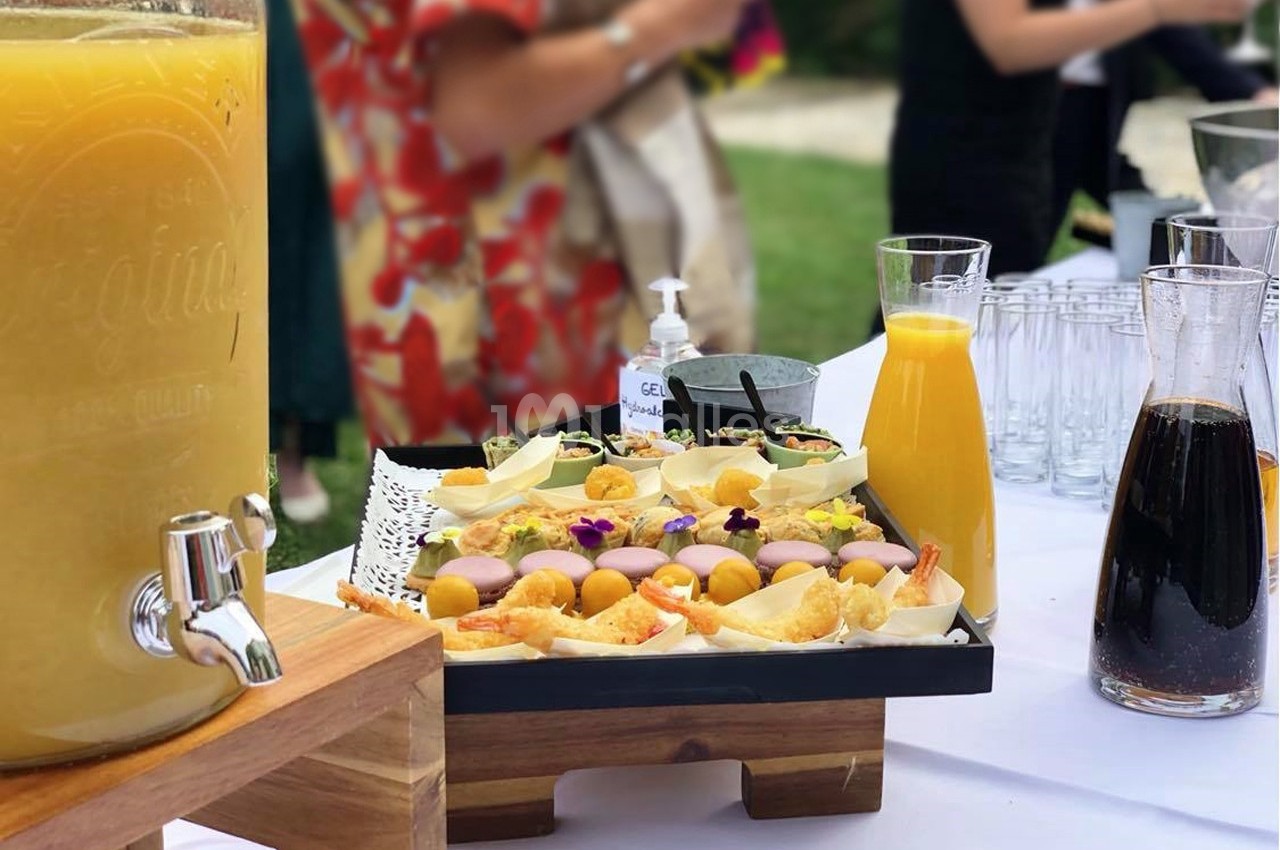 Buffet en extérieur avec jus d'orange, carafe de café, et plateau de bouchées décorées de fleurs comestibles.