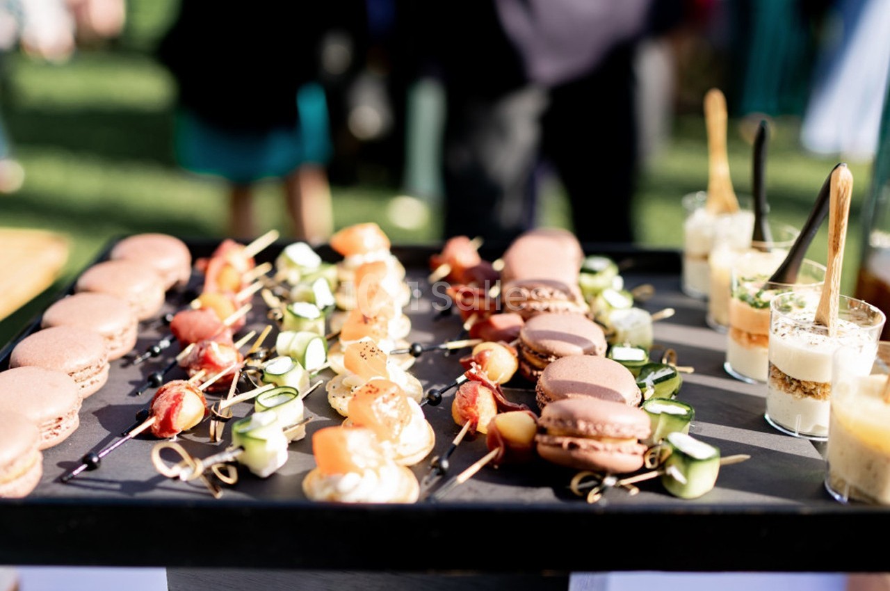 Plateau de bouchées apéritives variées comprenant macarons, brochettes de légumes et verrines, présenté en extérieur.