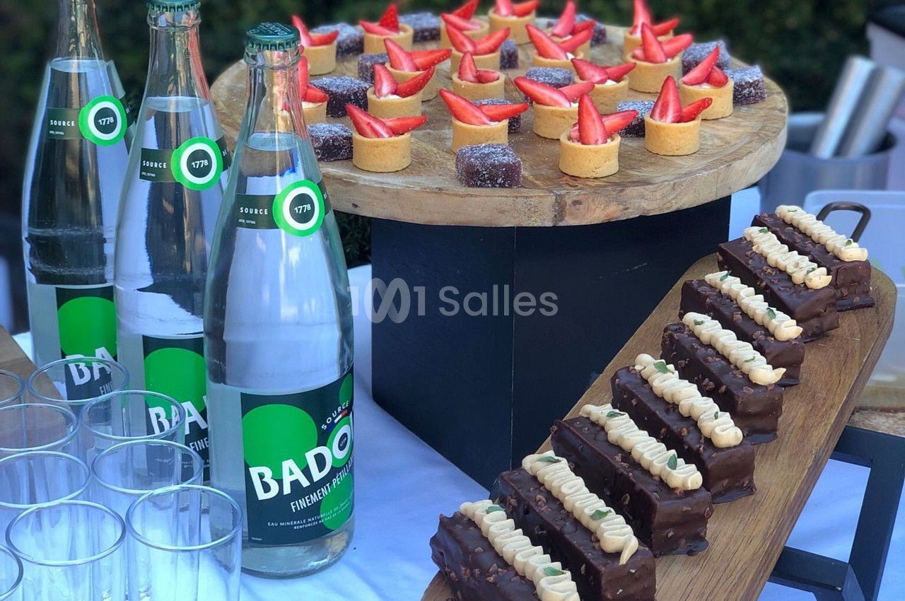 Plateau de desserts variés avec tartelettes aux fraises, gâteaux au chocolat et bouteilles d'eau minérale sur une table.