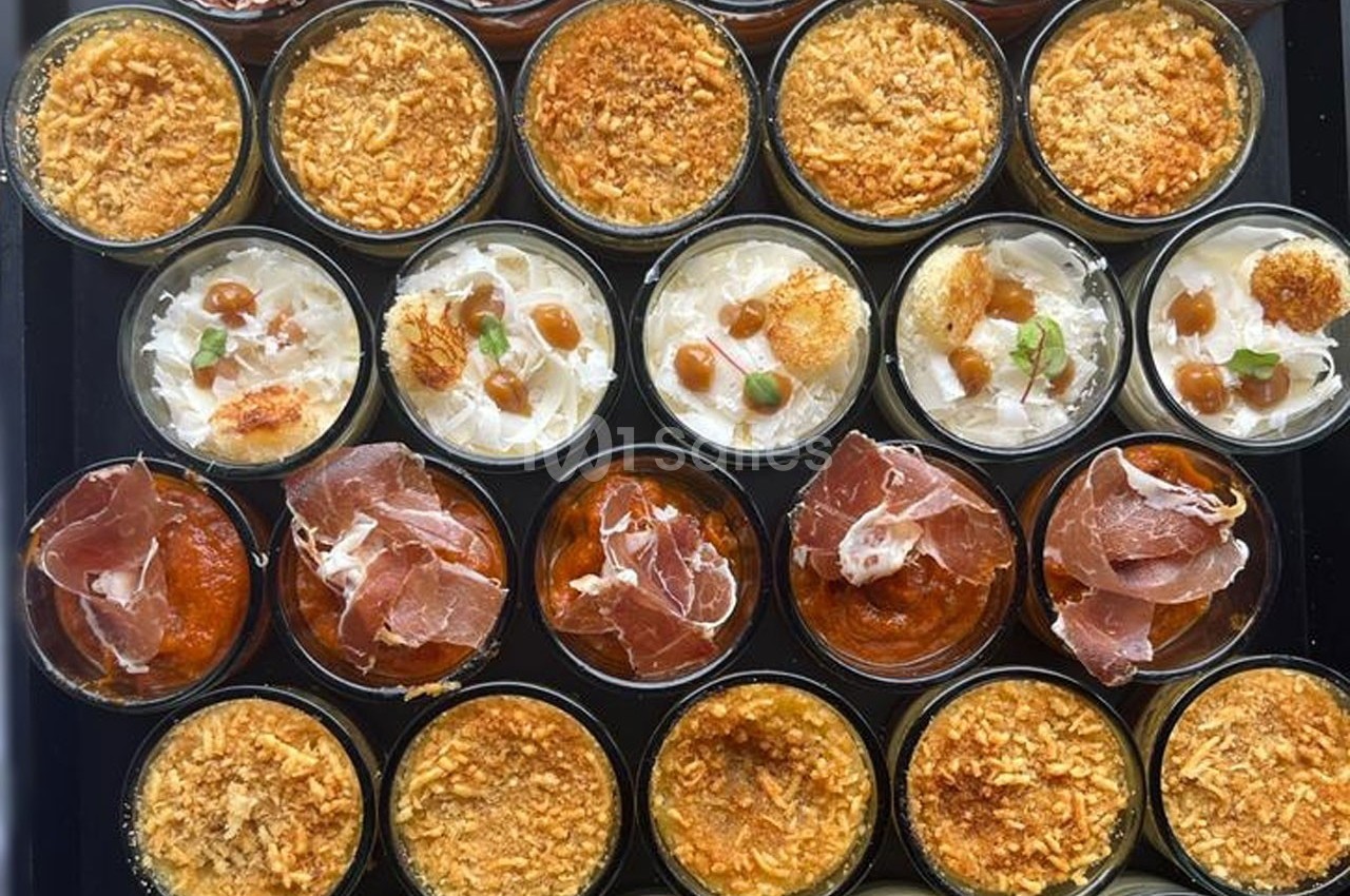 Assortiment de verrines salées garnies de jambon, fromage, sauces et miettes croustillantes, disposées sur un plateau.