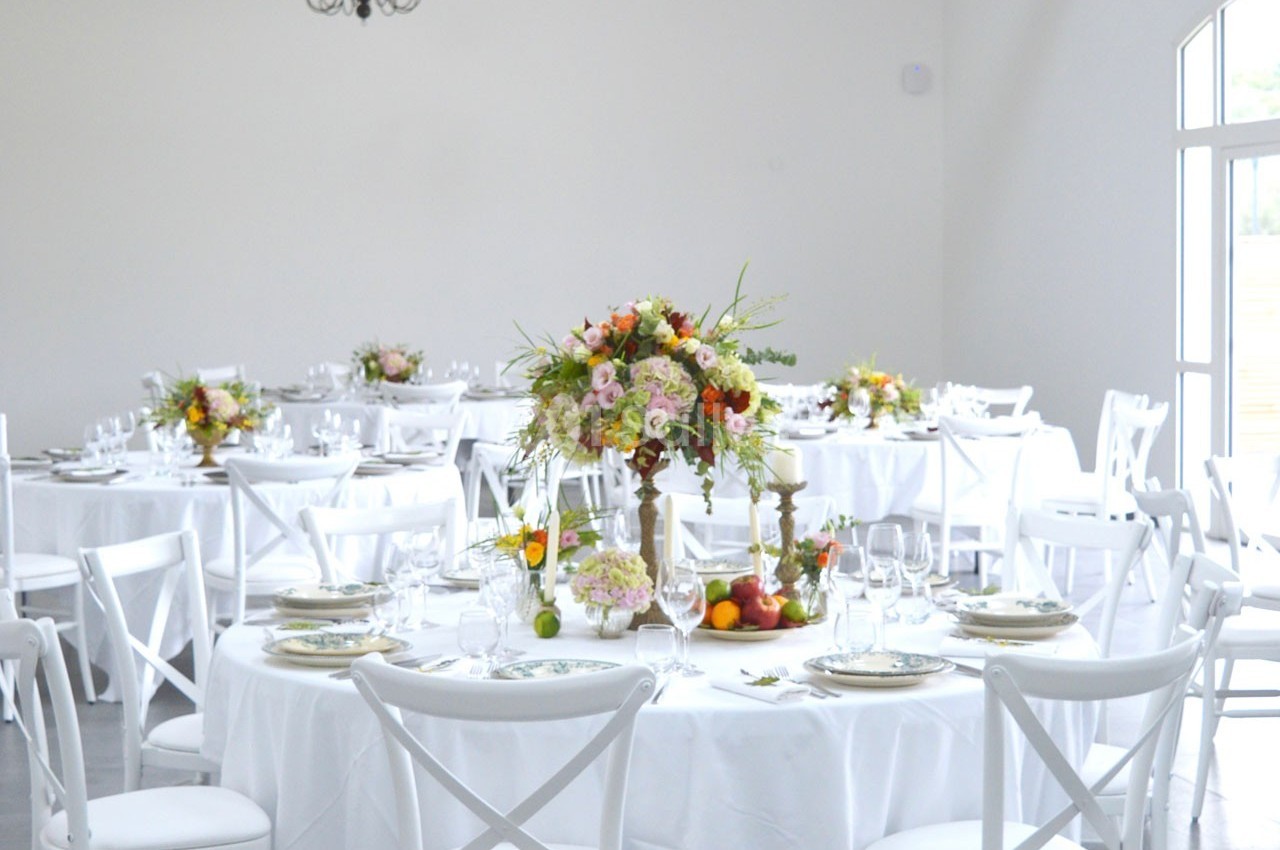 Salle lumineuse avec des tables rondes dressées, décorées de bouquets de fleurs colorées et de vaisselle élégante.