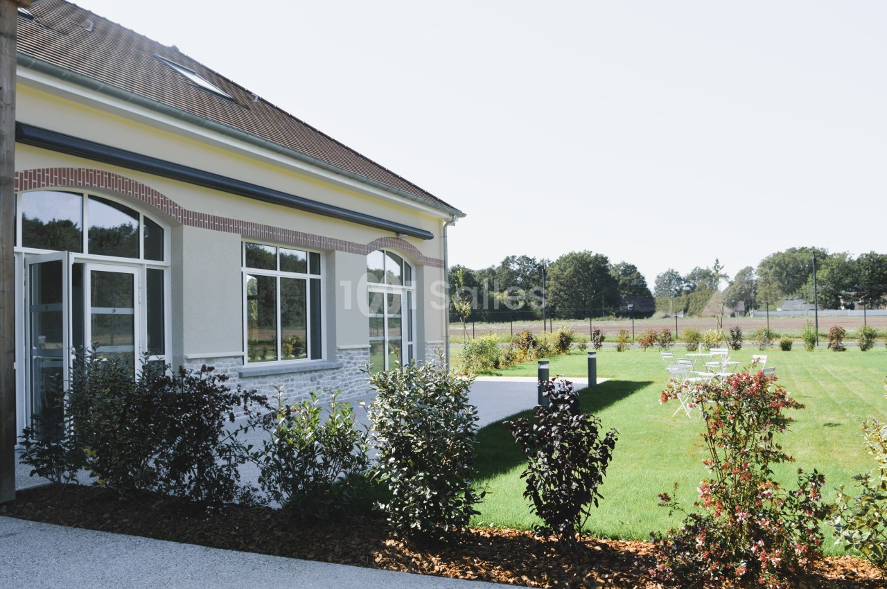 Bâtiment avec de grandes fenêtres donnant sur un jardin aménagé avec pelouse et quelques arbustes.