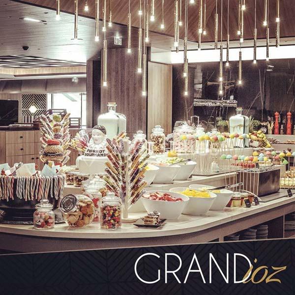 Buffet varié avec desserts, bonbons, fruits et décorations lumineuses dans un cadre moderne et élégant.