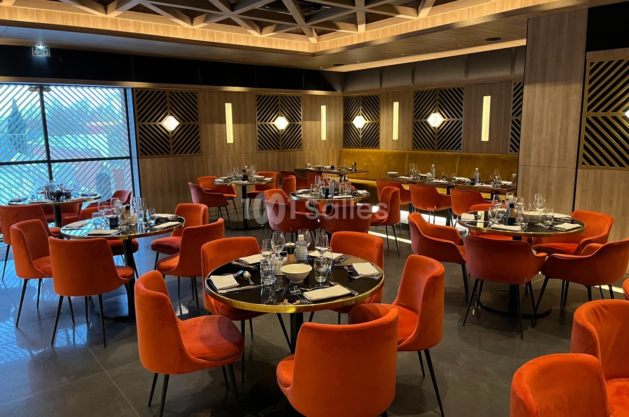 Salle de restaurant moderne avec des tables dressées, des chaises orange et un éclairage chaleureux.