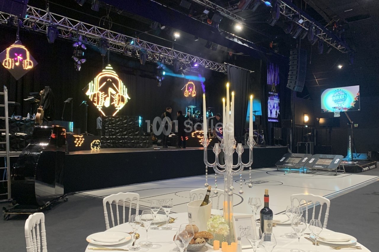 Salle de réception avec scène éclairée, table dressée au premier plan et décorations lumineuses en arrière-plan.