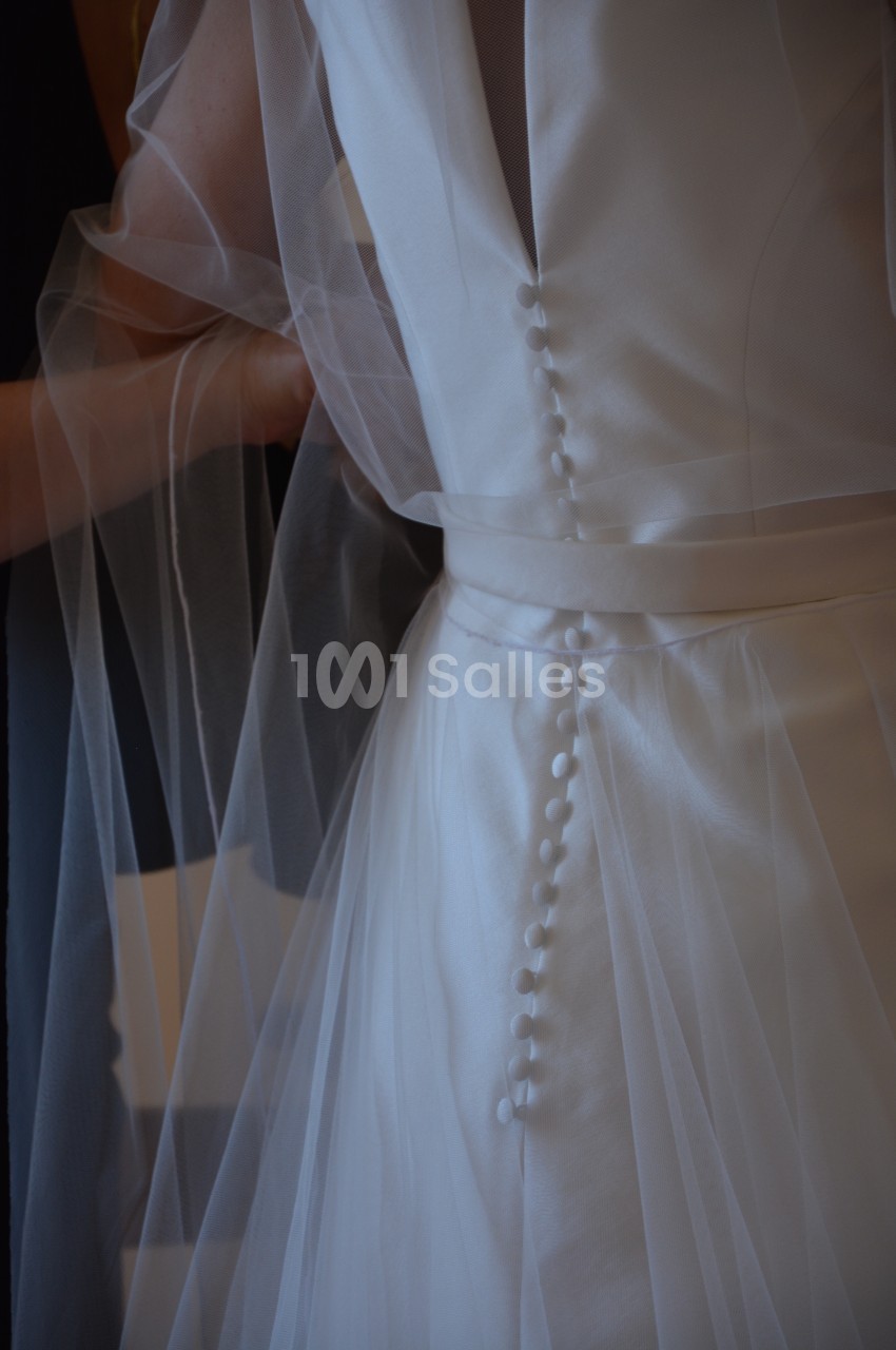 Robe de mariée en satin blanc avec boutons recouverts et voile transparent drapé.