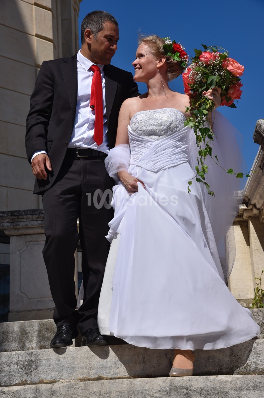 Un couple en tenue de mariage descend un escalier en pierre par une journée ensoleillée.