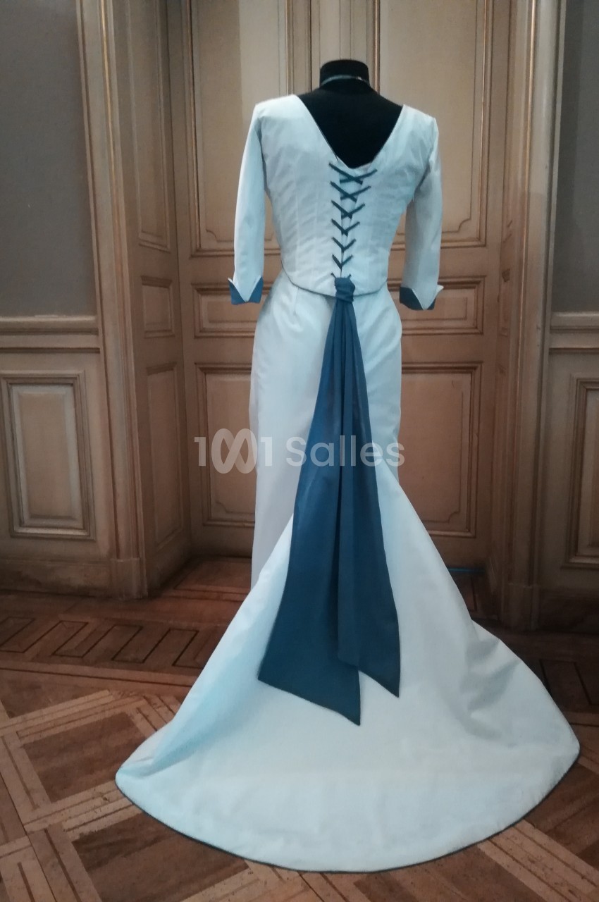 Robe blanche à manches longues avec un laçage au dos et une longue traîne bleue, présentée sur un mannequin.