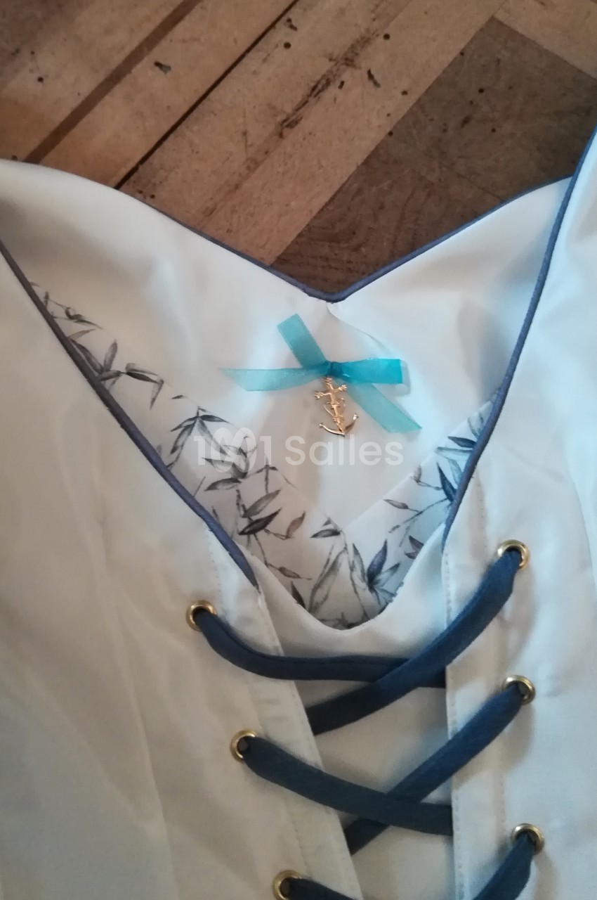 Corsage blanc avec laçage bleu, doublure imprimée de motifs végétaux et ornement en forme d'ancre marine.