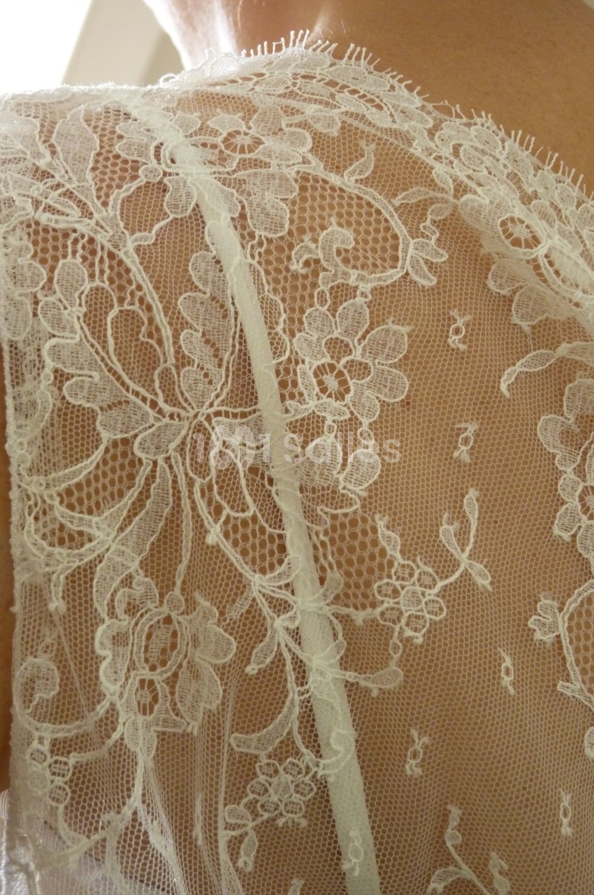 Dentelle blanche délicate avec motifs floraux portée sur une épaule.