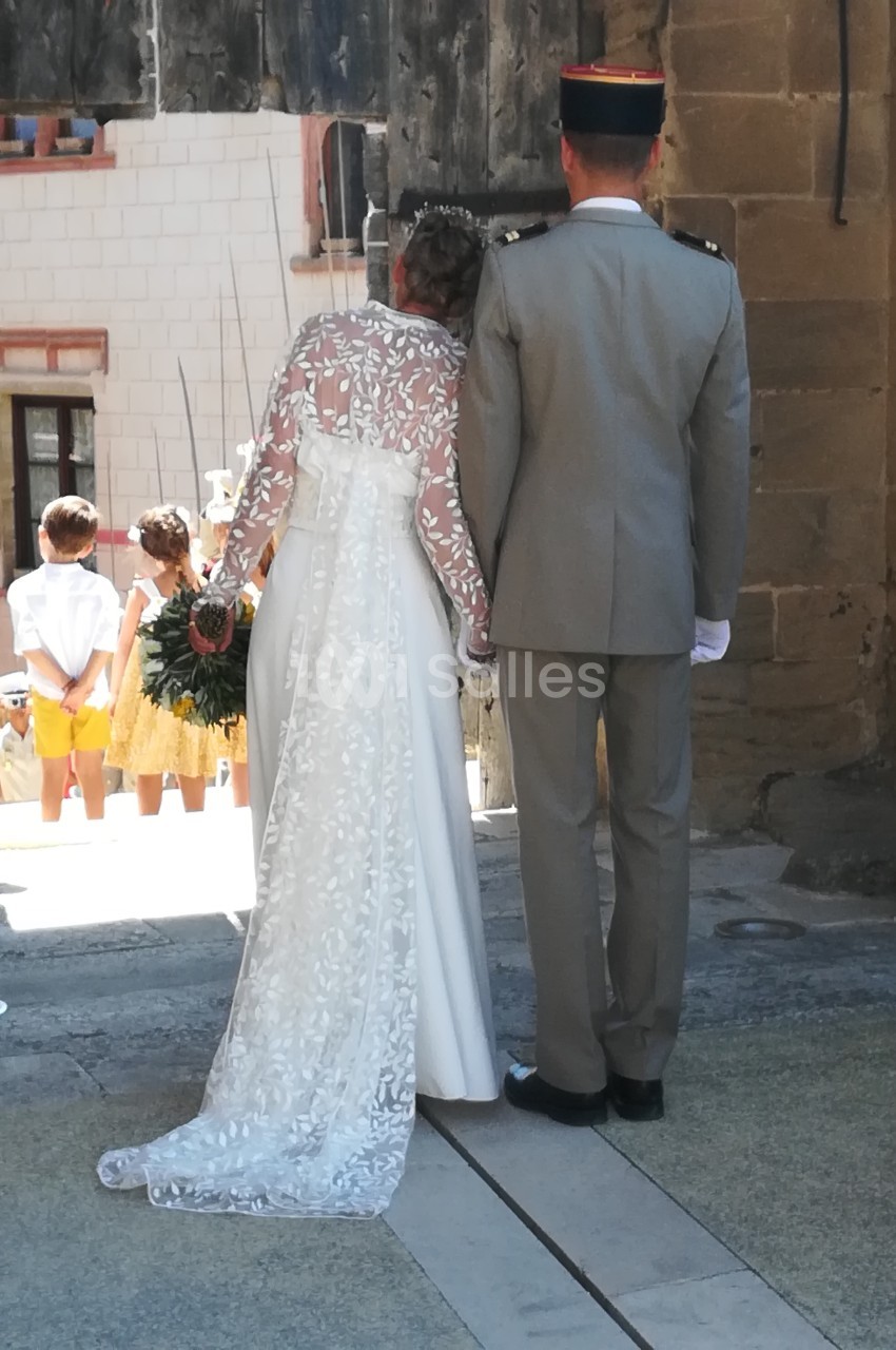 Un couple en tenue de mariage vu de dos, sortant d'un bâtiment ancien, avec des enfants en arrière-plan.