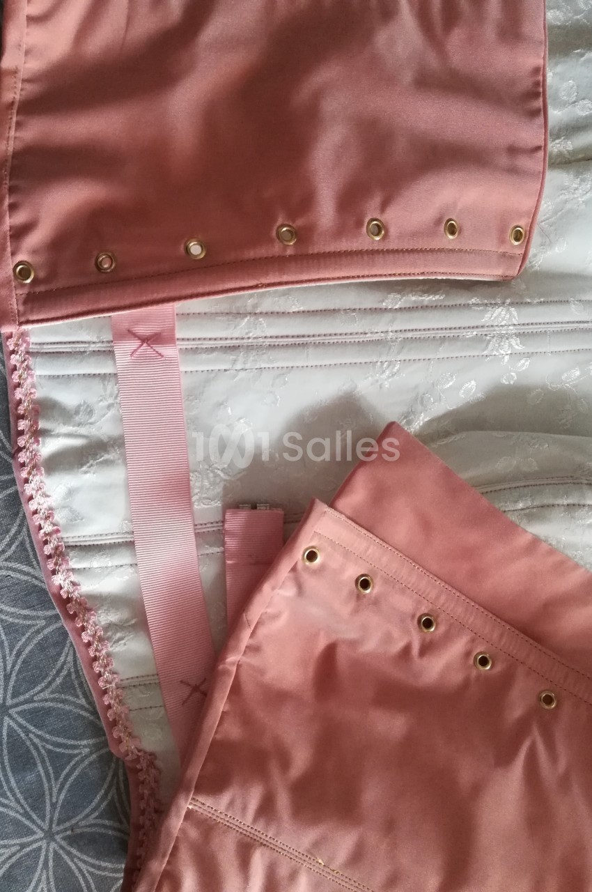 Vue rapprochée d'un corset rose en satin avec œillets dorés et rubans, posé sur un tissu à motifs.